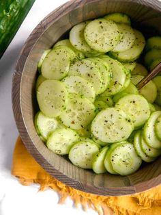 a wooden bowl filled with cucumbers on top of a white table next to a knife