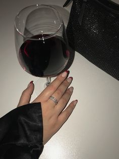 a woman's hand next to a glass of wine on a table with a black purse