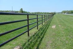 a black metal fence in the middle of a grassy field next to an empty road