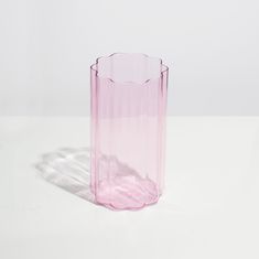 a pink glass vase sitting on top of a white table next to a shadow cast object