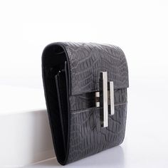 The Cinhetic design, which draws inspiration from moving Kinetic art, is rendered here as a square wallet surrounding an ingenious closure. When locked, the clasp resembles an H for Hermes, but when open, the pieces rotate into a sleek metal line. This extraordinary example is done in Matte Graphite Alligator with Palladium hardware, and features the super useful removable matching Alligator shoulder strap, and a small leather-bound mirror which fits perfectly into one of the wallet’s interior s Formal Compact Leather Clutch, Elegant Compact Business Wallets, Elegant Textured Leather Wallet, Elegant Textured Leather Rectangular Wallet, Luxury Clutch With Silver-tone Hardware, Modern Compact Wallets For Formal Use, Luxury Compact Wallet For Formal Occasions, Luxury Crocodile Pattern Business Wallets, Luxury Crocodile Pattern Wallet For Business