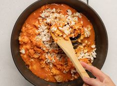 a person stirring food in a skillet with a wooden spoon on the counter top