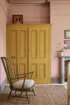 a yellow armoire sitting next to a white chair in a room with pink walls