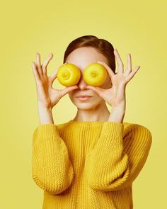 a woman holding two yellow donuts in front of her eyes