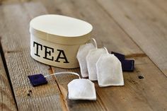 three tea bags sitting on top of a wooden table next to a white container with the word tea written on it