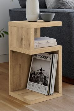 a table with magazines and a vase on it in front of a gray couch next to a grey sofa