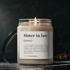 a candle sitting on top of a table next to a black mug with the words sister in law printed on it