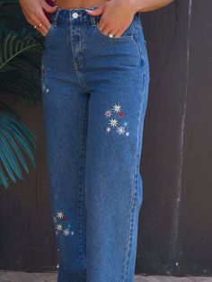 a woman is wearing jeans with flowers on them and has her hands in her pockets