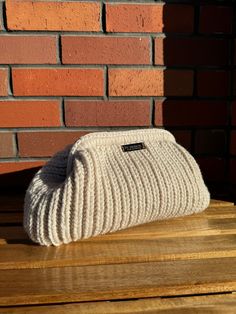 a white knitted purse sitting on top of a wooden table next to a brick wall