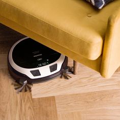 a roomba is sitting on the floor next to a yellow couch and throw pillows