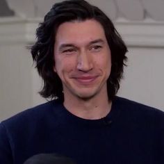 a man with long hair is smiling and holding a microphone in front of his face