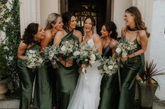 a group of women standing next to each other in front of a building holding bouquets