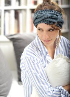 a woman in a blue and white striped shirt is holding a pillow while sitting on a couch