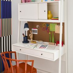 a desk with a chair, lamp and pictures on the wall behind it in front of a white bookcase