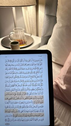 an open book sitting on top of a bed next to a table with a lamp