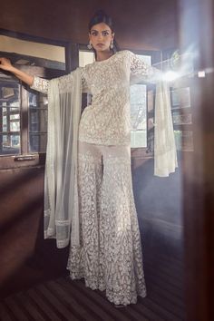 a woman standing in front of a window with her arms out and wearing white clothing