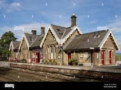 an old train station with red doors and windows on the side of the tracks - stock image