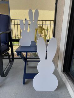 two paper rabbits sitting on top of a blue table next to a chair and window