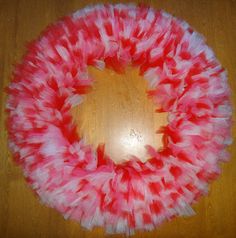 a pink and white feather wreath on top of a wooden table