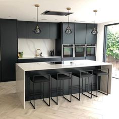 a large kitchen with black cabinets and white counter tops is pictured in this image, there are four stools at the center of the island