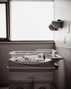 a black and white photo of a baby in a crib next to a window