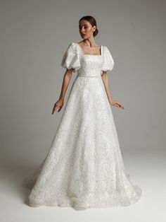 a woman in a white wedding dress standing on a gray background with her hands behind her back