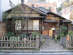 an old house with a wooden fence in front of it and some plants growing on the outside