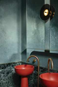 two red bowls sit on the counter in front of a mirror, with gold faucets