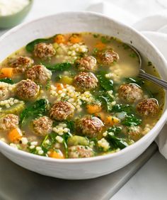 a white bowl filled with meatball soup on top of a table next to a spoon