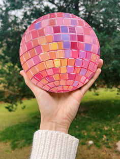 a person holding up a pink and orange mosaic ball in front of a green field