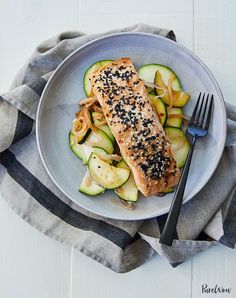 a white plate topped with salmon and zucchini salad next to a fork on top of a towel