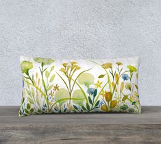 a rectangular pillow with watercolor flowers on it sitting on a wooden table in front of a white wall