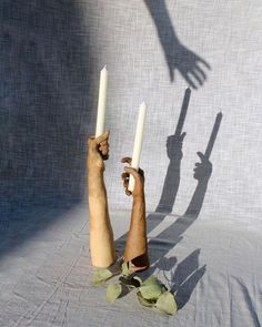 two hands holding candles in front of the shadow of a person's hand on a sheet