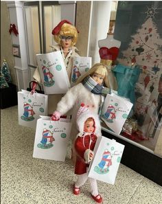 two barbie dolls are holding shopping bags in front of a christmas tree