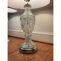 a glass table lamp sitting on top of a hard wood floor next to a wall