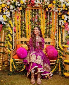 a woman sitting on top of a wooden bench covered in flowers and garlanded with lights