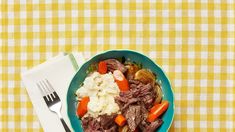 a blue bowl filled with meat and vegetables on top of a yellow checkered table cloth