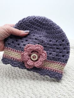 a hand is holding a crocheted hat with a flower on the front and side