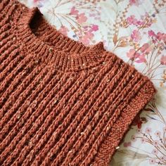 an orange knitted sweater laying on top of a flowered bed sheet with pink flowers