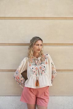 This blouse features a modern Mayan-inspired Floral/ emblem embroidery and trim stylish design. Its balloon-style long sleeves and tasseled front closure make it an ideal piece to pair with fitted tops, such as crop tops, brami's, and tanks, combined with jeans or shorts. Model is 5' 9" and wearing a size small. White Embroidered Cropped Blouse, Feminine Floral Embroidery Button-up Top, Chic Floral Embroidery Button-up Top, Embroidered Cream Button-up Top, Bohemian Embroidered Off-white Blouse, Emblem Embroidery, Embroidery Blouse, Floral Embroidery, Top Blouse