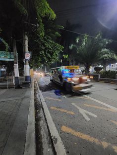 a car driving down the street at night time with lights on and trees in the background