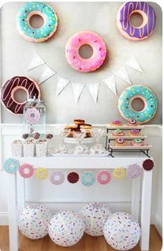 there are donuts hanging on the wall behind a white table with pink, blue and green doughnuts