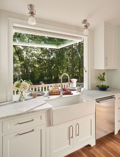 a kitchen with white cabinets and an island in front of a large window that looks out onto the backyard