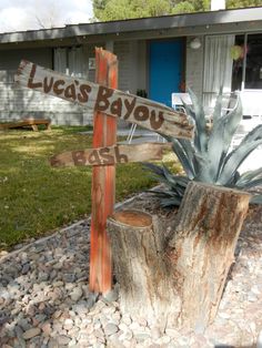 a wooden sign sitting on top of a tree stump in front of a house with grass and rocks around it