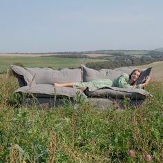 a woman laying on top of a couch in the middle of a field next to tall grass