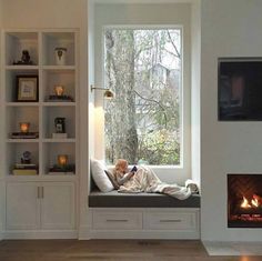 a person sitting on a window seat in front of a fire place with bookshelves