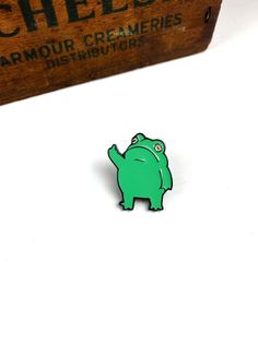 a small green animal pin sitting on top of a white table next to a wooden box