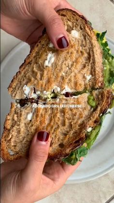 a hand holding a sandwich with lettuce, cheese and tomato on it in front of a white plate