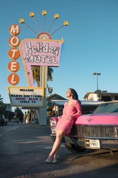 a woman leaning on the hood of a pink car in front of a motel sign