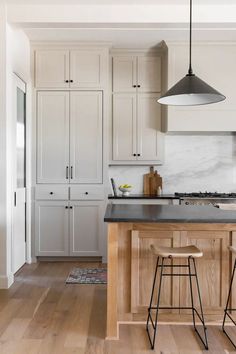 a kitchen with white cabinets and black counter tops, two stools in front of the island